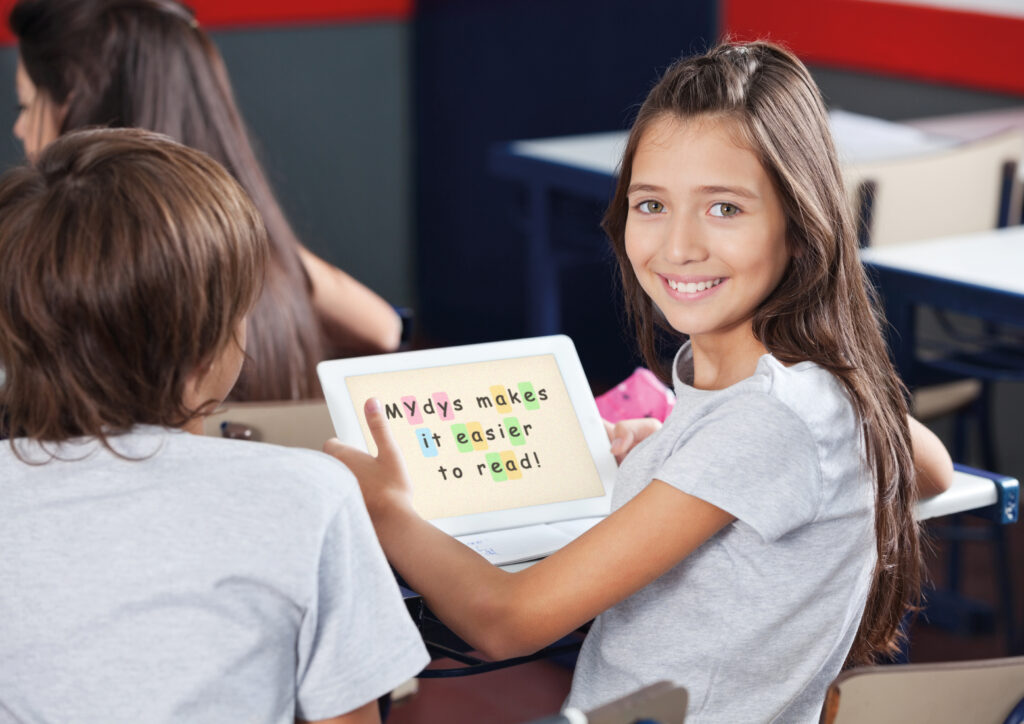 Ecolière souriante qui tient une tablette entre ses mains avec la mention "MYdys makes it easier to read!"